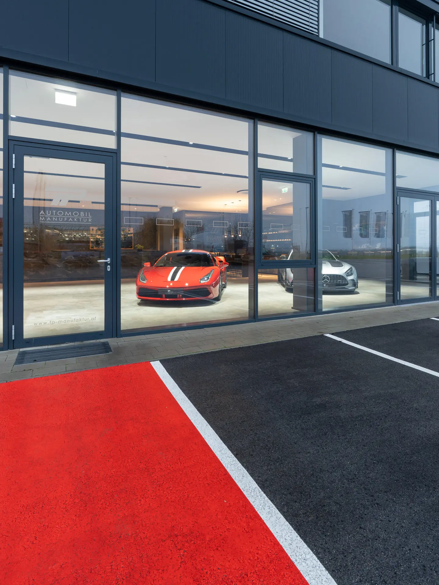 Glass facade exterior of TP Automobil Manufaktur showroom at dusk